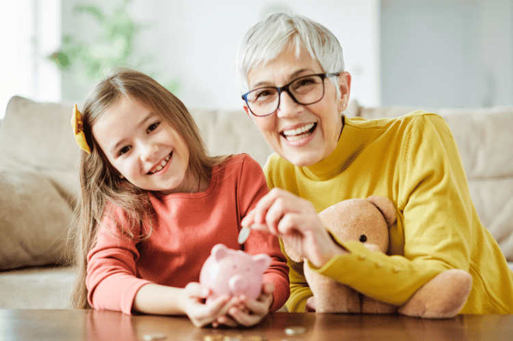 Grandmother and granddaughter smiling while putting coins into a piggy bank