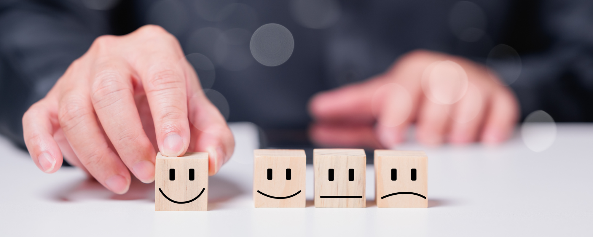 Image of wooden blocks with diffent expressions. A finger points to the one that is smiling.